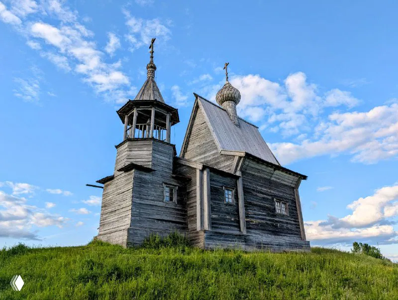 Купол и колокольня Никольской часовни крупным планом: резная деревянная архитектура на фоне ясного голубого летнего неба