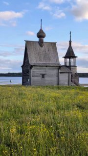 Вертикальный вид Никольской часовни среди цветущего луга у озера: деревянные формы и сельский ландшафт Кенозерского нацпарка