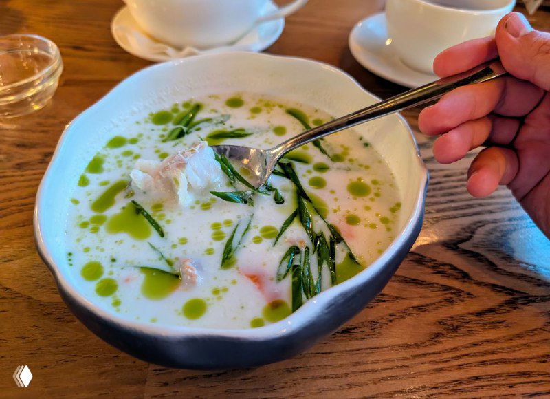 Тарелка с северным супом: светлый бульон, зелёные масляные капли и кусочки рыбы в аккуратной подаче авторской кухни ресторана.