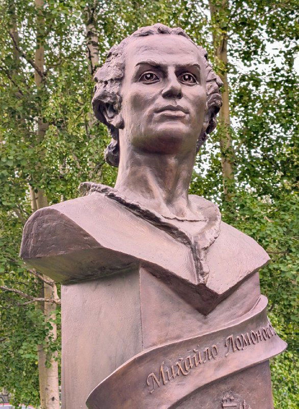 Бюст Михаила Ломоносова на фоне зелёных берёз рядом с дорогой к музею в Ломоносово, памятник вблизи главного села на Курострове.