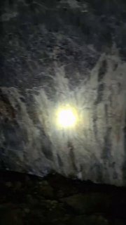 Интерьер пещеры Шульган‑Таш: свет фонарика, блики и темная каменная поверхность с видимыми контурами древних рисунков и карстовой текстурой.