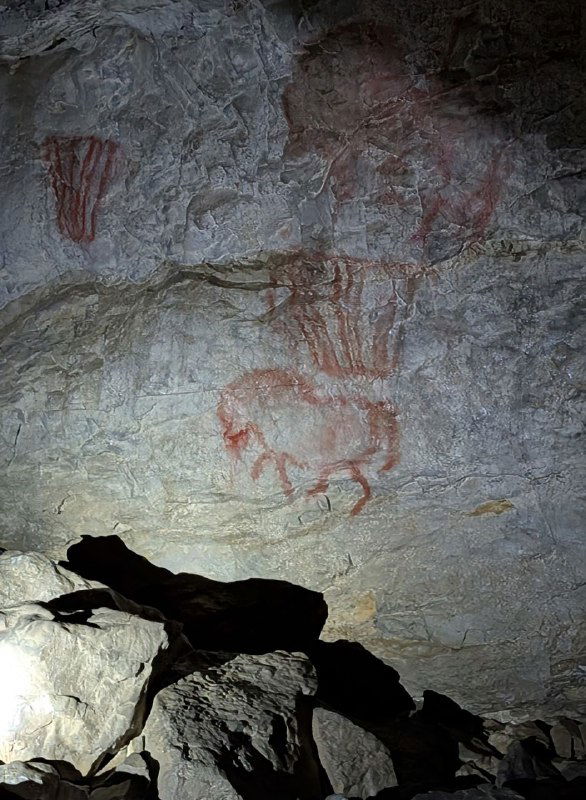 Стена с несколькими красными палеолитическими изображениями в Шульган‑Таш: группы символов и схематичных животных, видна техника рисования охрой на камне.