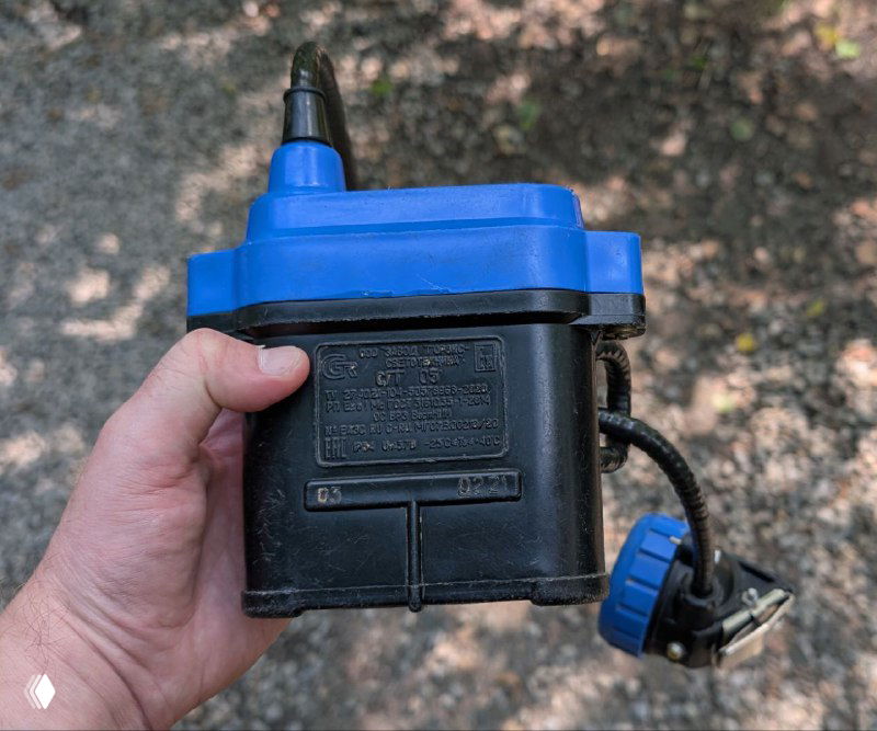 Ручной электрический насос или компактный прибор в руке автора на фоне лесной тропы — предмет походного инвентаря, использованный в поездке к пещере.