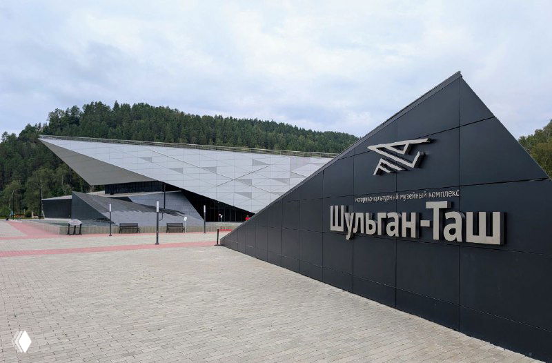 Фасад музейного комплекса Шульган‑Таш с современной архитектурой и крупной надписью «Шульган‑Таш» у входа, вид на инфоцентр и площадку перед зданием.