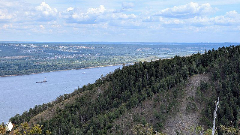 Панорама Волги и крутой лесистый склон Жигулёвских гор, вид с тропы ниже вершины горы Стрельной, удалённые баржи и противоположный берег.