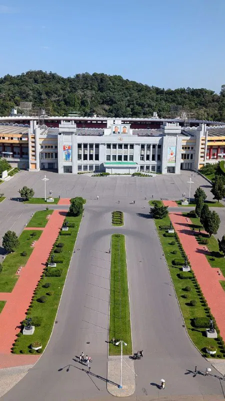 Вид с высоты: парадная аллея и административные здания перед аркой, аккуратные дорожки и симметричная озеленённая композиция внизу.