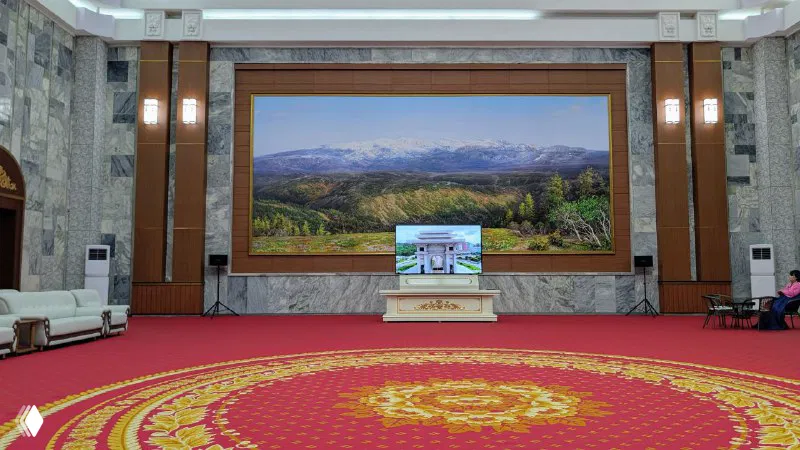 Внутренний зал арки с красочным ковровым покрытием, большим экраном для показа фильма и картиной на стене — просторный официальный интерьер.