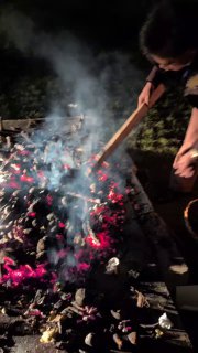 Человек разравнивает угли и раскладывает горячие угли после костра, рядом видны остающиеся угли и посуда — сцена пикника.