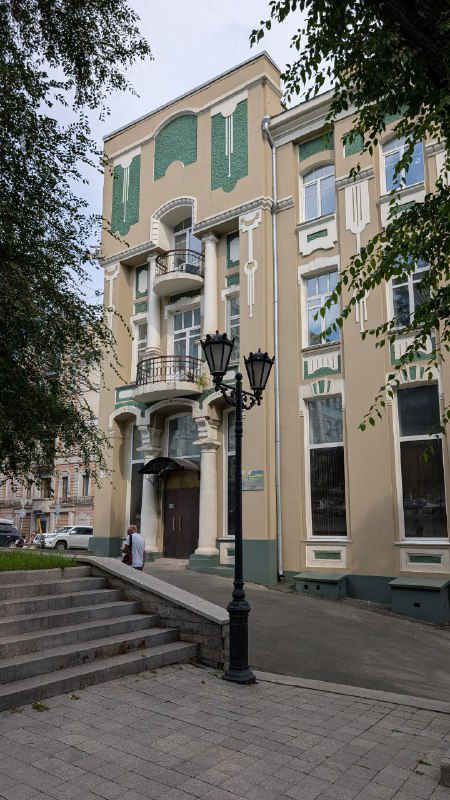 Пастельно-окрашенный жилой дом во Владивостоке с декоративными фасадными элементами и уличными фонарями, дневной снимок фасада.