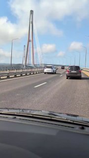 Движение по Золотому мосту снято из салона машины: авто на проезжей части, дорожное полотно и вид на сталежелезные пилоны моста.