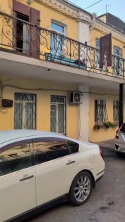 Фасад низкого дома во дворе Миллионки с балконом, решётками и кондиционером, припаркованная белая машина на переднем плане.