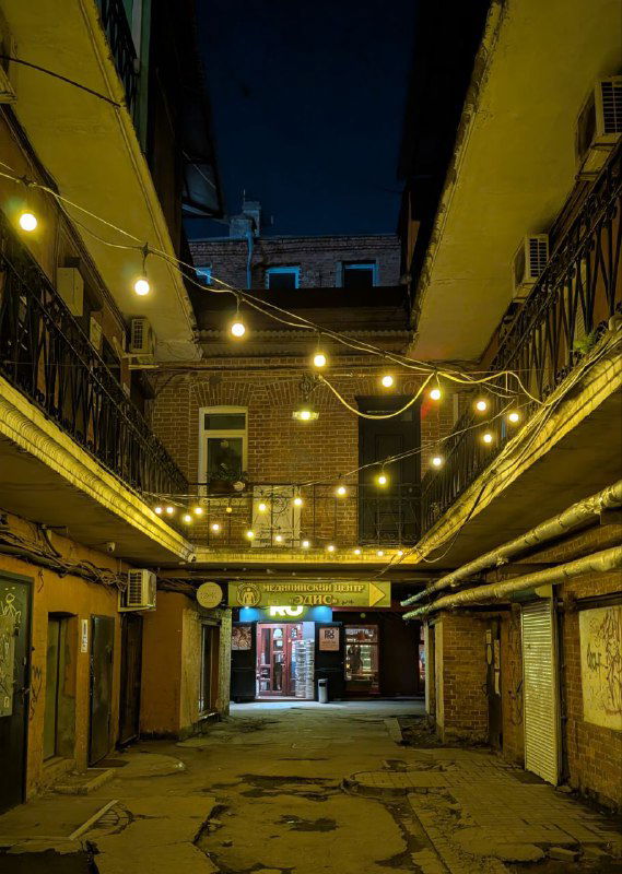 Ночной двор Миллионки с гирляндой тёплого света и арочными конструкциями — подсвеченные переходы создают кинематографичную атмосферу.