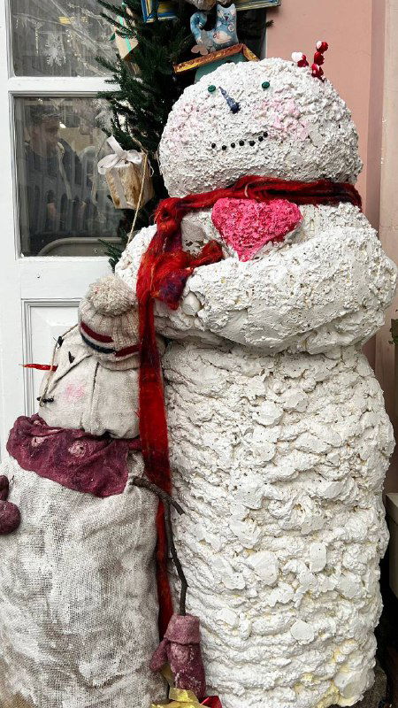 Снеговик из декоративных материалов у дверей кофейни — крупный текстурный арт‑объект с шарфом и фактурой искусственного «снега», детали на переднем плане.