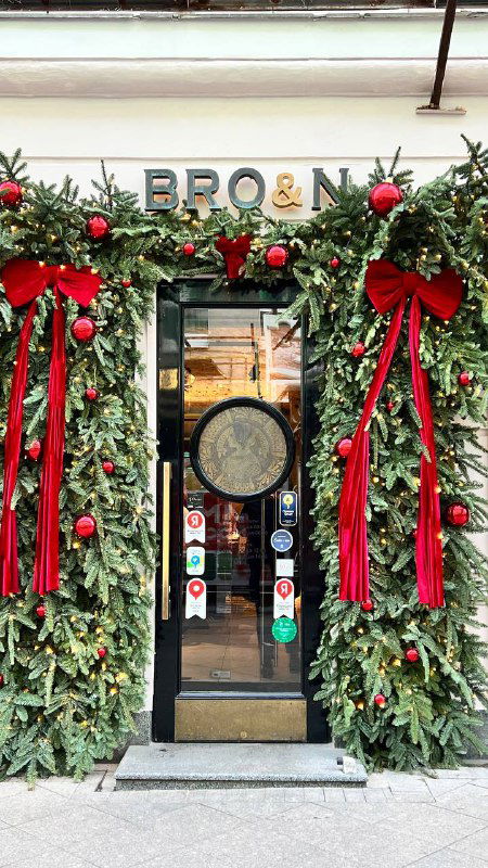 Вход в магазин, украшенный рождественской гирляндой и красными бантами — праздничная витрина в городском центре, фасад в сезонном декоре.