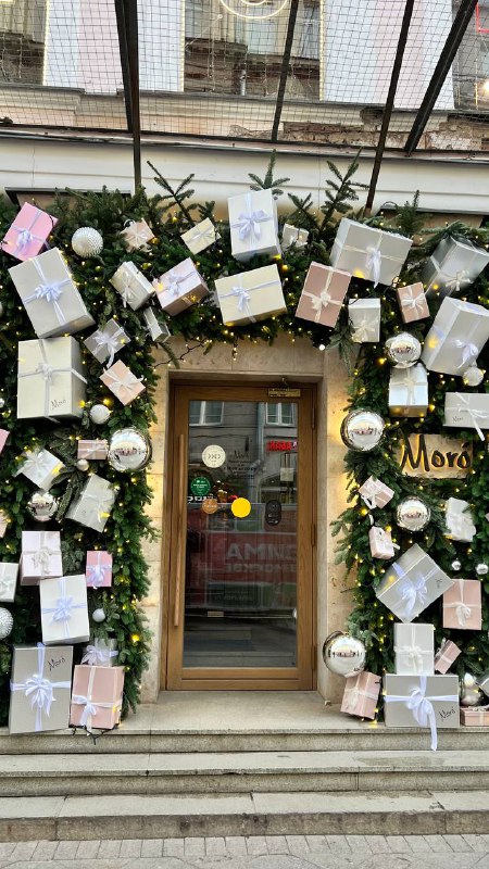 Дверной проём, усыпанный гирляндой и множеством подарочных коробок — креативная праздничная инсталляция на фасаде, зрительный акцент для прохожих.