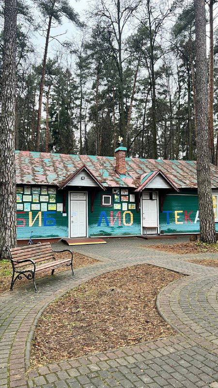 Небольшой расписной домик-музей среди сосен в Переделкино: окрашенный фасад, тропинка, лавочка и окружение парка, создающее камерную атмосферу.