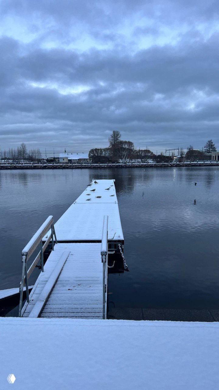 Деревянный причал, покрытый первым снегом, выходит в залив Салаккалахти на спокойной воде под низким серым небом.