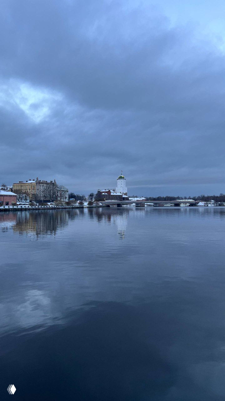 Вид через залив на Выборгский замок и главную башню святого Олафа: отражение в воде и приглушённая северная палитра.