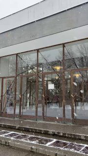 Большие стеклянные витрины и деревянные рамы главного входа библиотеки Аалто; видны отражения интерьера и снег на ступенях, акцент на прозрачности.