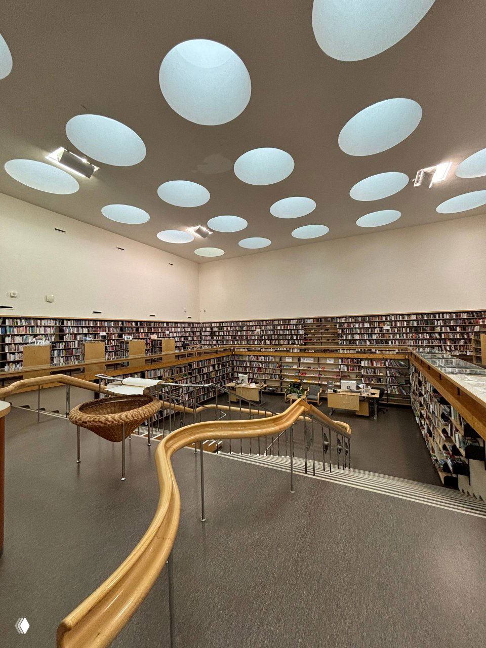 Панорамный кадр читального зала с множеством круглых световых люков, широкими полками с книгами и изогнутой деревянной перилой лестницы — внимание к эргономике.