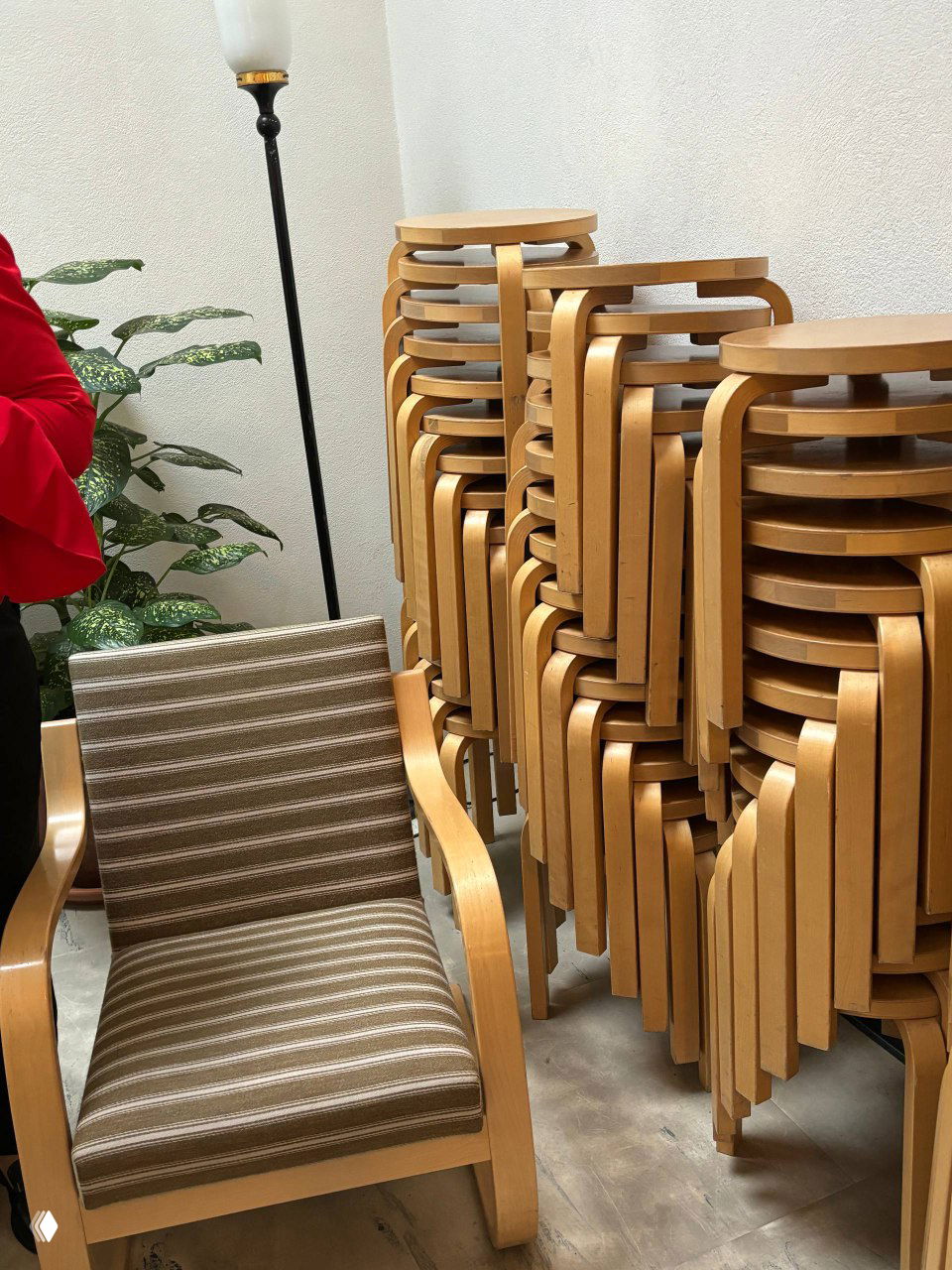 Штабелированные табуретки и кресло по дизайну Аалто в углу: примеры функциональной мебели, удобной для быстрой перестановки и хранения в общественном пространстве.