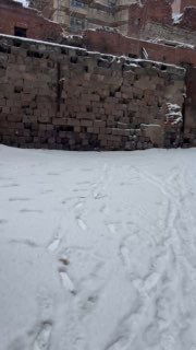 Снежный двор с мощёной площадкой и высокой каменной крепостной стеной Выборга, следы на снегу и тихая зимняя сцена.