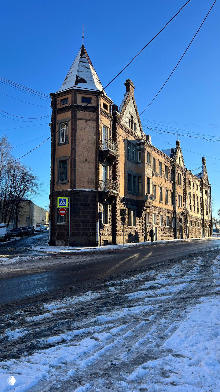 Улица Выборга с характерными старинными домами и солнечным светом на фасадах; на тротуаре видна прохожая в зимней одежде.