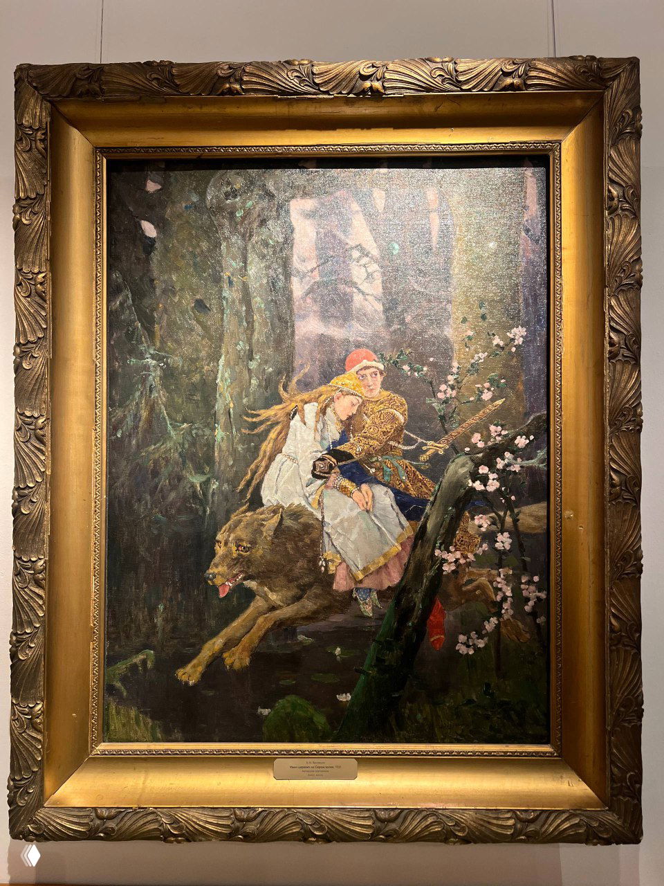 Рамочная живопись в золотой раме на светлом фоне: сцена с парой и лесным пейзажем, характерная манера Васнецова в цветовой гамме.