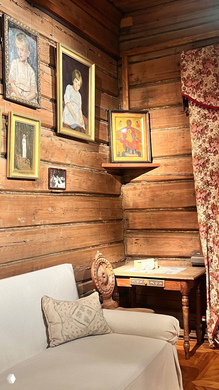 Уютный музейный уголок с диваном, столом и иконой на полке; деревянные стены и тёплая экспозиционная атмосфера.