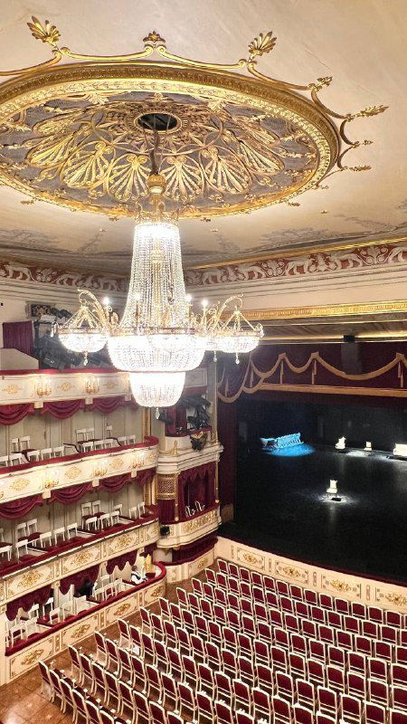 Роскошная люстра и расписной потолок зрительного зала Малого театра; вид на бельэтаж, бархатные ложи и оформленную сцену из верхней точки зрения.