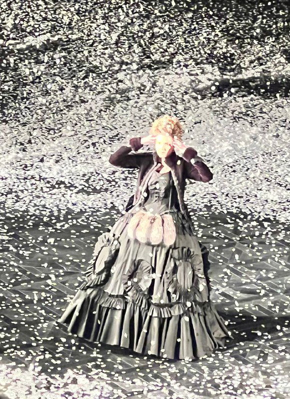 Крупный план актрисы в пышном историческом платье под падающим бумажным снегом; видны детализированные костюмы и выразительное лицо персонажа.