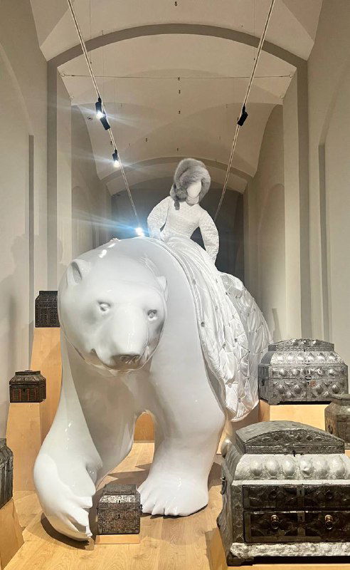 Скульптурная композиция: белый медведь с фигурой в платье на спине на фоне музейного зала — сочетание ткани и монументальности в инсталляции.