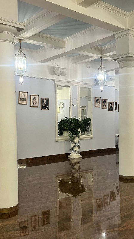 Фойе сцены на Ордынке: колонны, белые стены, мраморные полы и фотографии на стенах — спокойный зал перед спектаклем с отражениями на полу.