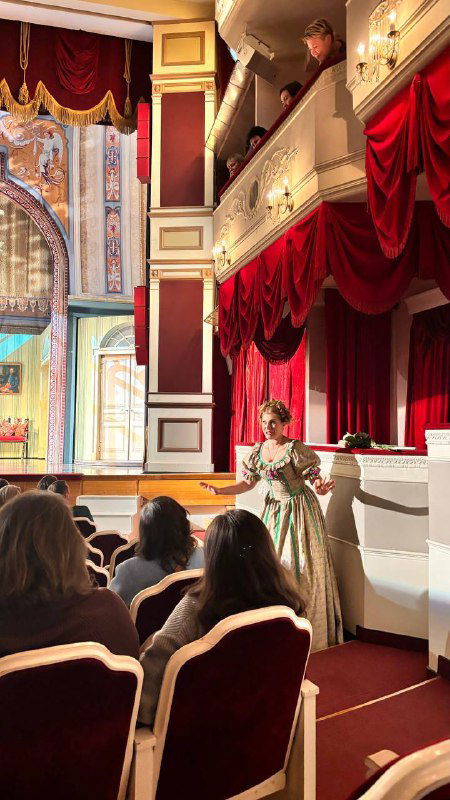 Сцена и зрители из партерного уровня: актриса у борта сцены, красные шторы и частично занятые места — момент спектакля в малом зале.