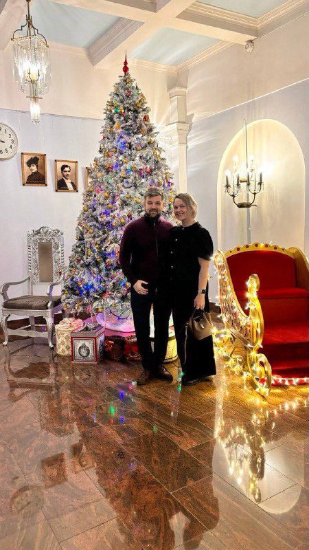 Пара у рождественской ёлки и декоративной инсталляции в фойе Малого театра: праздничная атмосфера в зале во время предпраздничного показа.