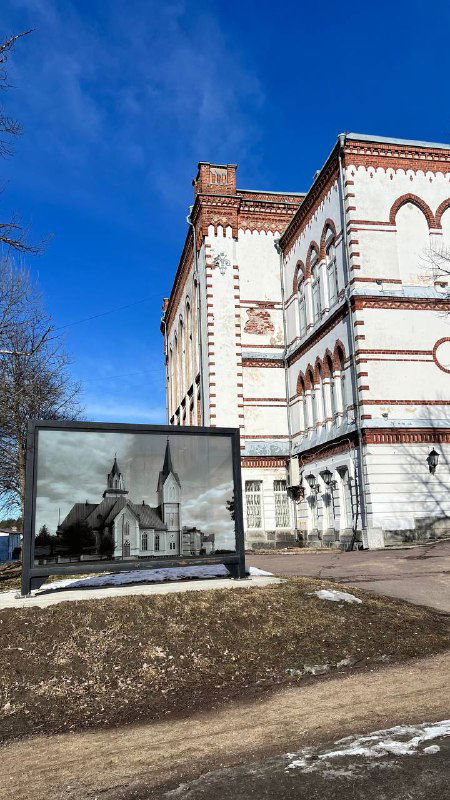 Фасад исторического здания и чёрно‑белая фотография на штендере — памятный уголок архитектуры Сортавалы конца XIX — начала XX века.