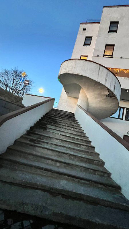 Белая наружная винтовая лестница современного здания — контраст современной формы и исторической застройки Сортавалы на фоне неба.