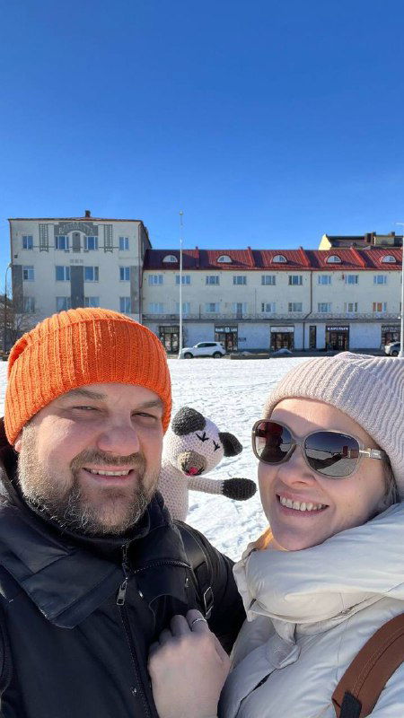Селфи мужчины и женщины на снегу у зданий Сортавалы; на переднем плане видна часть игрушки и тёплая одежда пары в ясный морозный день.