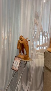 Интерьер экспозиции: скульптура с лестницей и персонажем, бензопильная резьба в современном стиле, вид на витрину выставки.