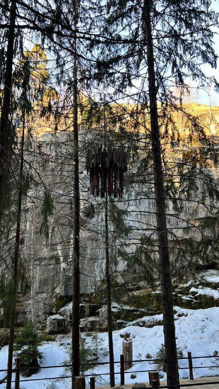 Вертикальная скалистая формация и металлическая конструкция на фоне деревьев, художественный акцент в природном ландшафте Паасо.