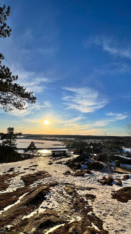 Солнце низко над горизонтом, ледяные поверхности и отражения на воде Ладоги, холодный вечерный свет над пейзажем.