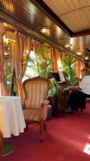 Ресторанный салон поезда с креслами в бархатной обивке, занавесками и зелёными растениями — интерьер VIP‑вагона с живой музыкой.