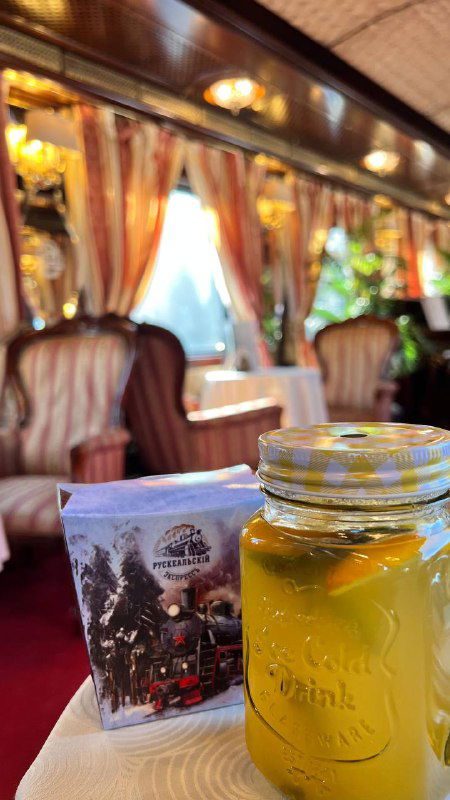 Баночка с мёдом и упаковка сувенира на столике в вагоне; крупный план на мелкие атрибуты поездки и спокойную сервировку.