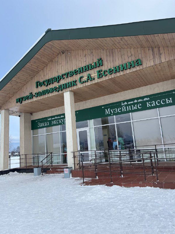 Фасад Государственного музея-заповедника С.А. Есенина зимой: вход, стеклянные кассы и снег у крыльца на фоне бледного неба.
