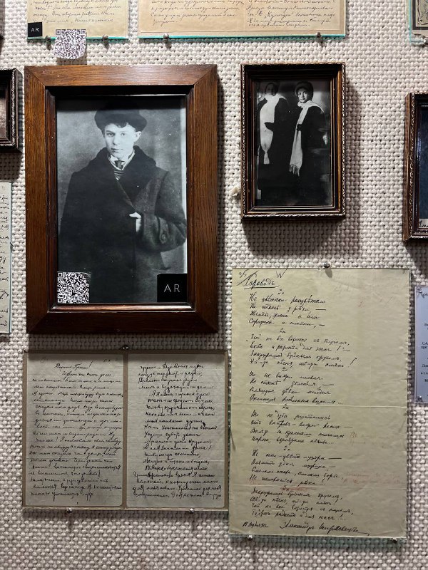 Фотографии и рукописи в рамке на стене музейного зала: старые портреты, листы с почерком и музейные подписи рядом друг с другом.