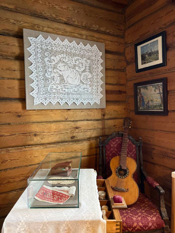 Интерьер деревянного дома-музея: традиционная мебель, кружевная скатерть, стул и шестиструнная гитара как часть домашней обстановки.