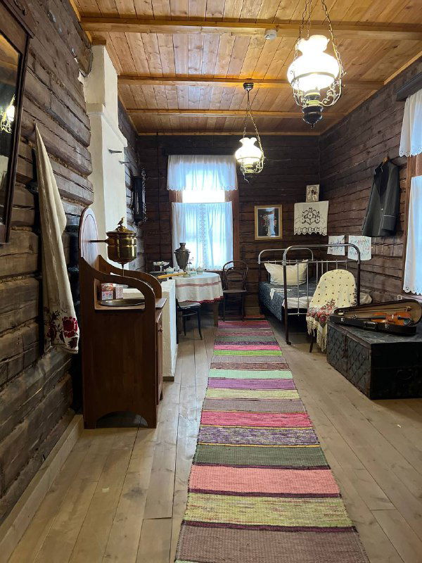 Комната в доме-музее с деревянной отделкой: кровать, коврики, сундуки и лампы — планировка и быт начала XX века.