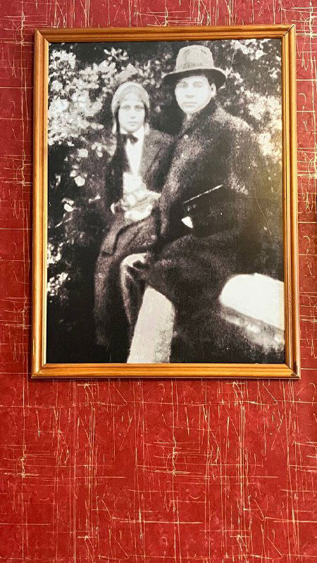 Чёрно-белый портрет в золотой раме на красном фоне: старое фото, вероятно родственников или современников поэта, в галерее музея.