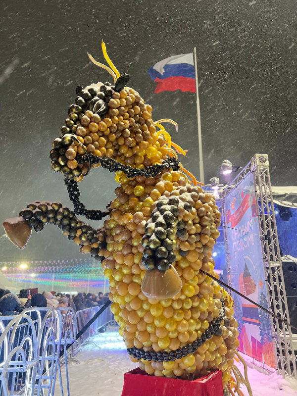 Праздничная декоративная скульптура, составленная из шаров и гирлянд, на фоне флага России и праздничной иллюминации в Туле зимой.