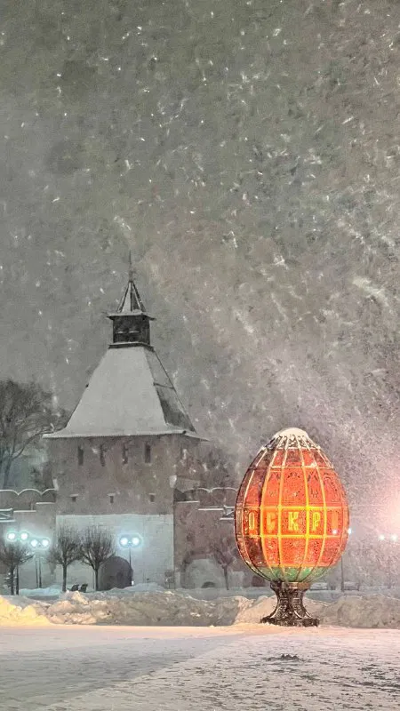 Сильный снегопад в Туле: заснеженные скульптуры и огни на площади, вечером видна часть исторической застройки и светящиеся инсталляции.